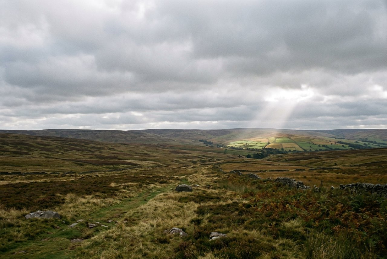 Four in the afternoon: a wide moor under heavy cloud with one shaft of light on a distant slope
