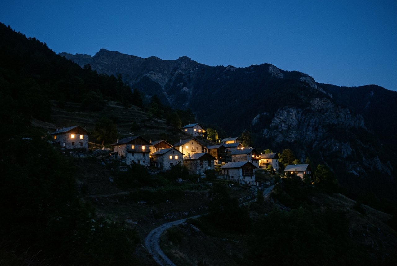 Ten at night: a mountain village of a dozen lit windows on a dark slope, deep blue sky with the ridge line still visible